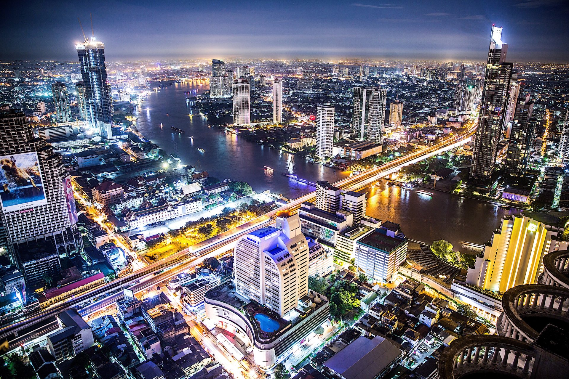 blick auf die metropole bangkok bei nacht mit beleuchteten hochhäusern und schillernden straßenzügen durchquert vom großen fluß